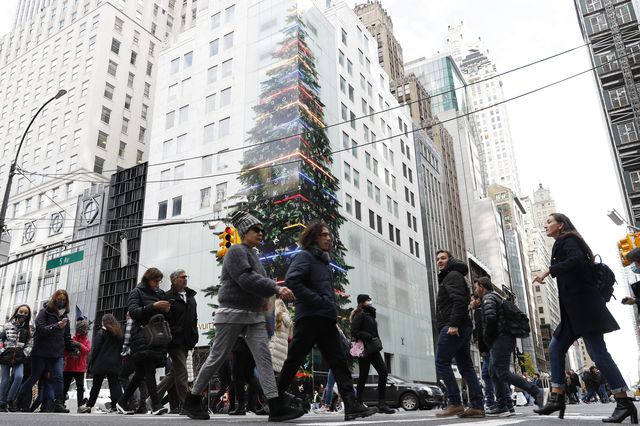 Pedestrians crossing a street in midtown Manhattan, with a building behind them decorated with a Christmas tree decal